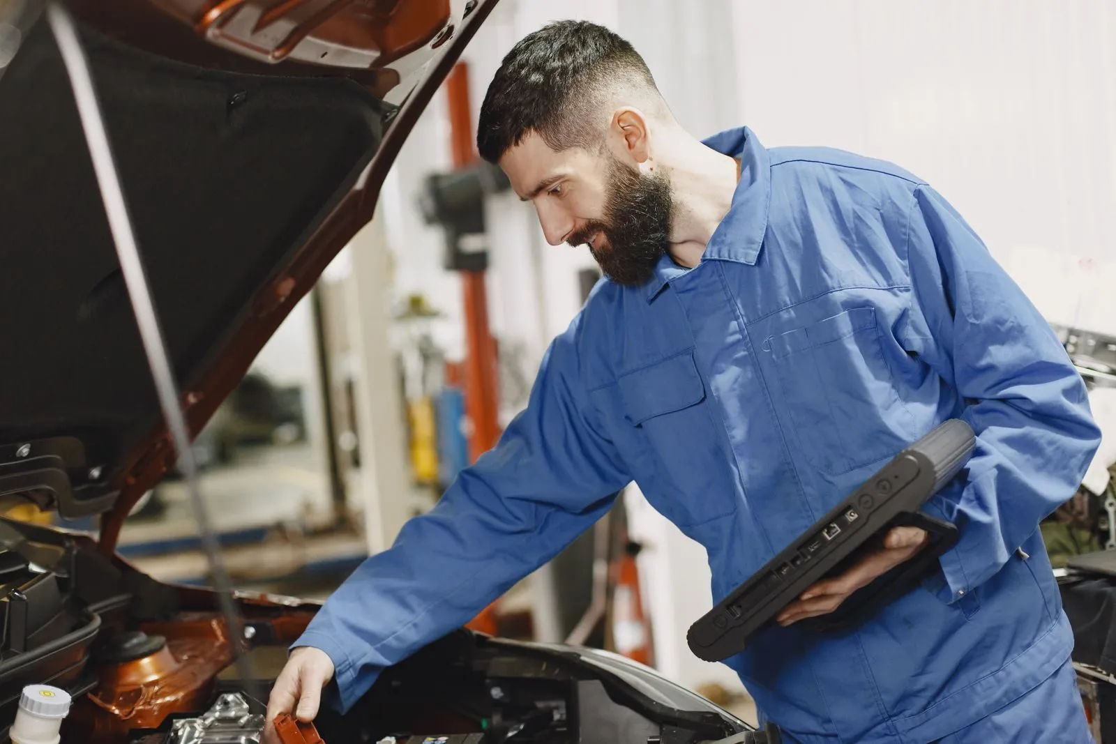 A mechanic in coveralls checking a vehicle with a tablet