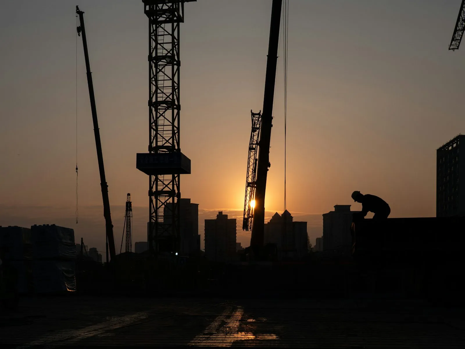 Construction cranes against a sunset sky