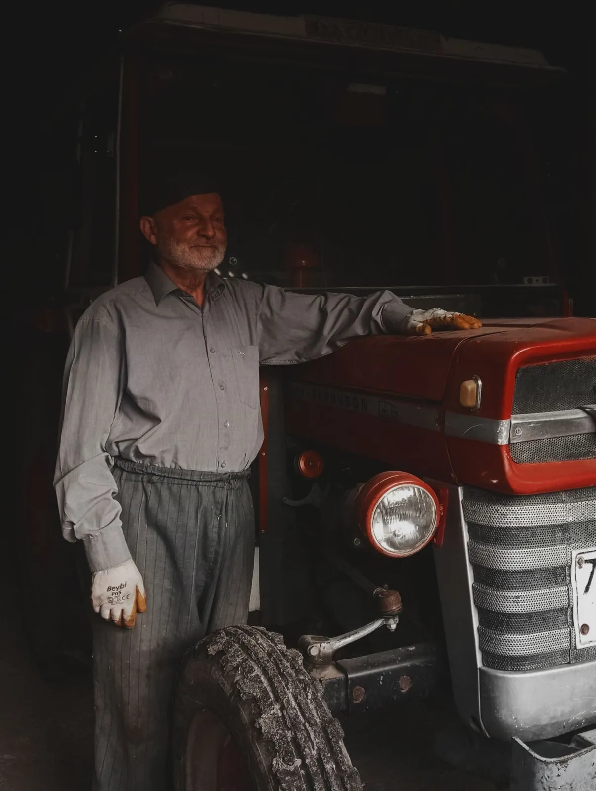 A farmer in work gloves with his hand on his well-used tractor inside a barn