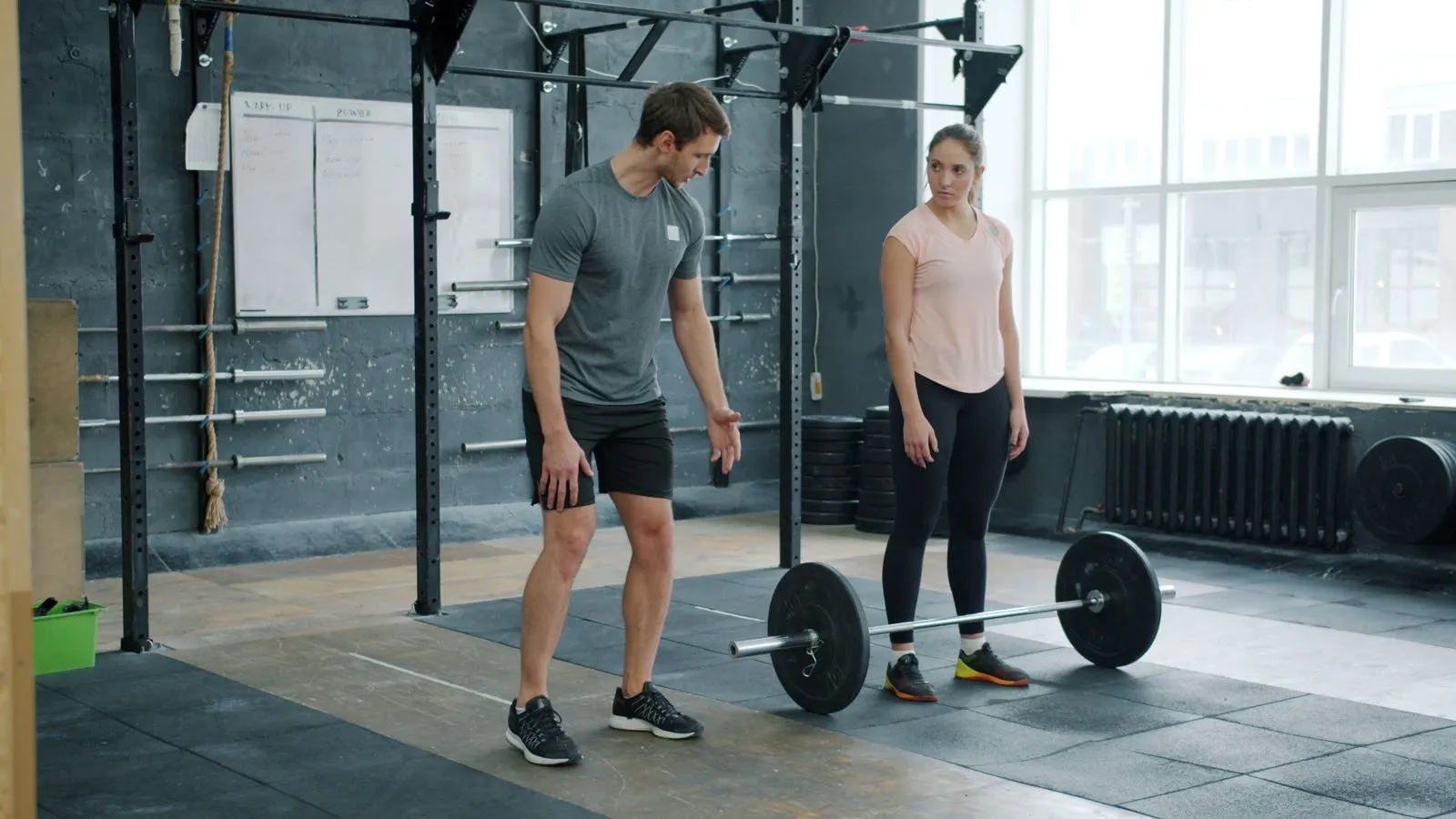 A trainer coaching a client at a barbell rack in a commercial gym