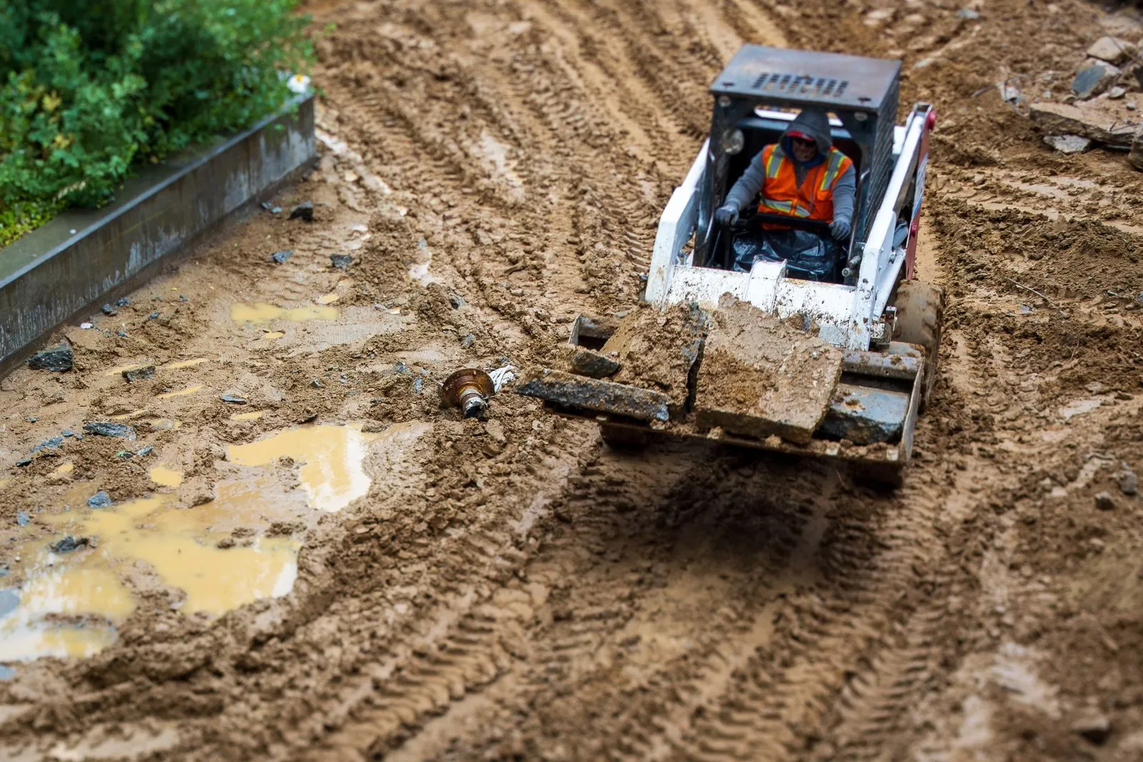 A skid steer operator moving material on a muddy site