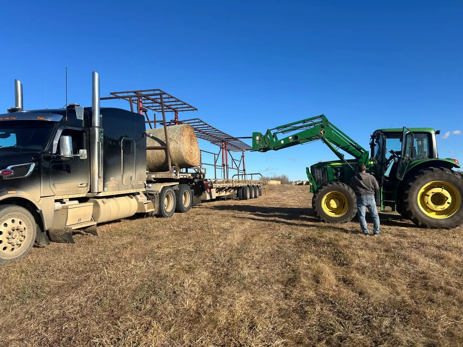 A flatbed trailer being loaded with hay bales on the prairie