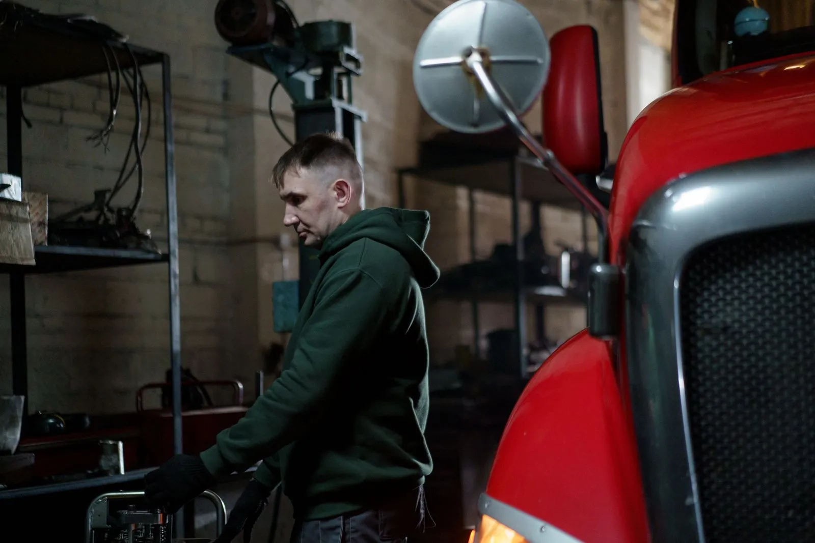 A mechanic inspecting the front of a red truck in a repair garage