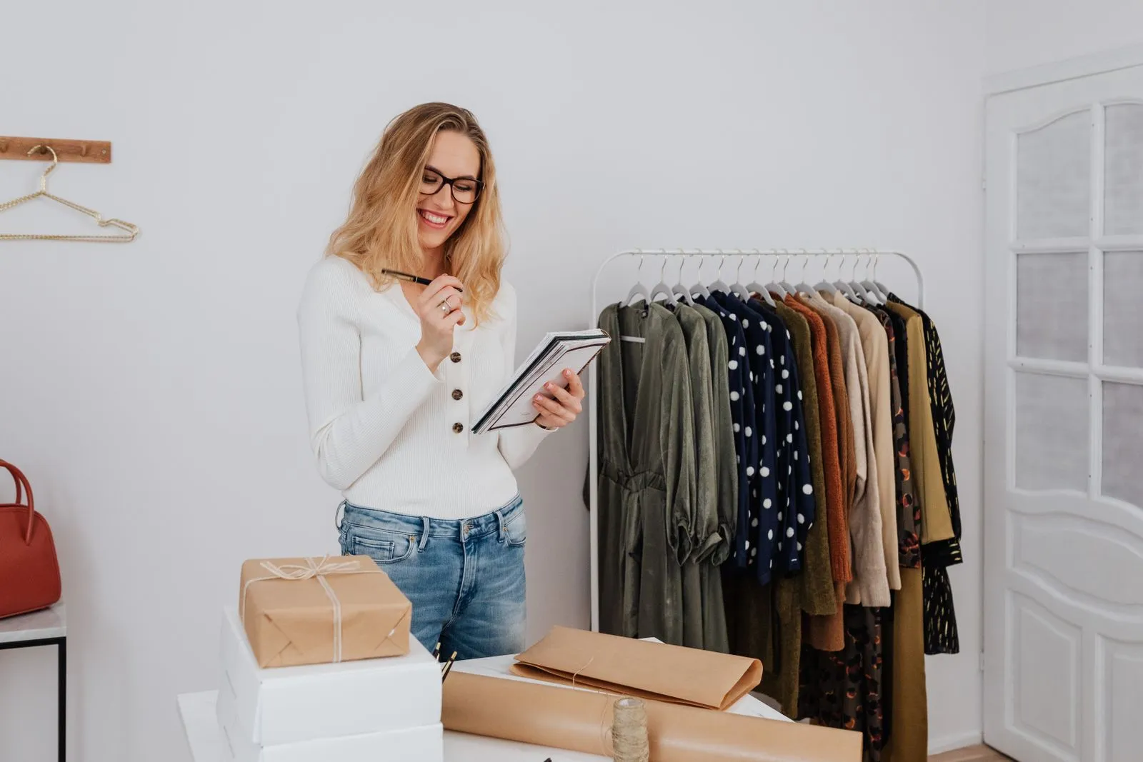 A boutique owner with a notepad taking stock beside a clothing rack and wrapped parcels